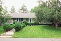 a house that is in the grass with trees and bushes on either side of it