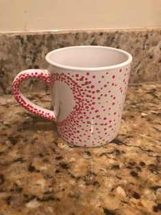 a white coffee cup with red polka dots on it sitting on a counter next to a wall