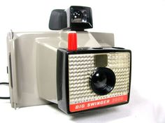 an old fashioned camera sitting on top of a white table next to a black and red object