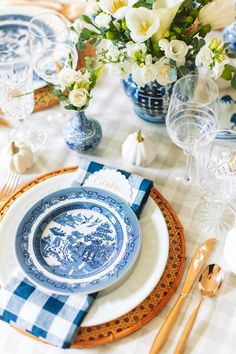 a blue and white table setting with flowers in vases on the side, gold cutlery