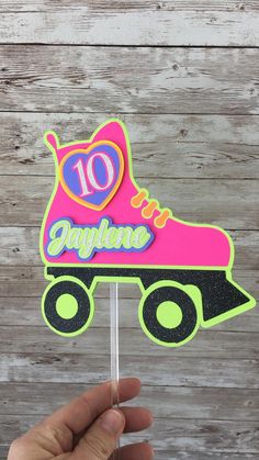 a hand holding up a pink roller skate cake topper with the number ten on it