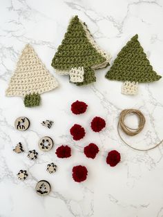 crocheted christmas trees and buttons on a marble counter top, with yarn in the middle