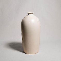 a white ceramic vase sitting on top of a table next to a gray wall and floor