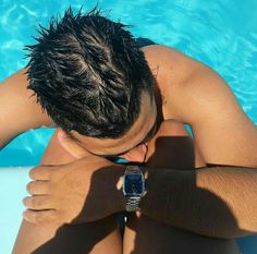 a man wearing a watch sitting in the water with his hands on his chest, looking down