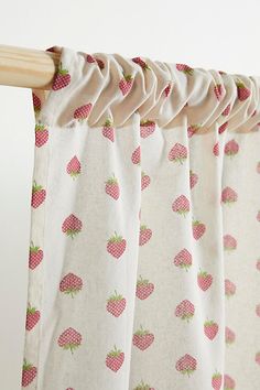 a curtain with pink and green strawberries printed on it, hanging from a wooden rod