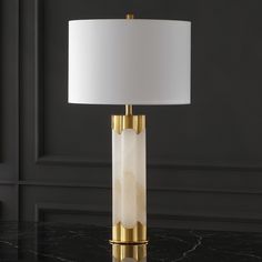 a table lamp with a white shade on it and a black wall in the background