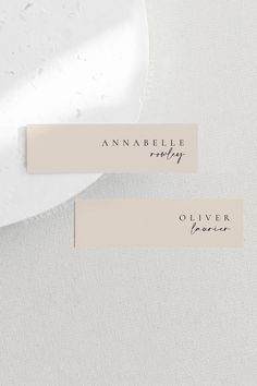 two place cards with names on them sitting next to a white plate and napkins