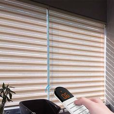 a person holding a remote control in front of a window with blinds on the outside