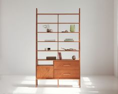 a wooden shelf with books and vases on it next to a window in a white room