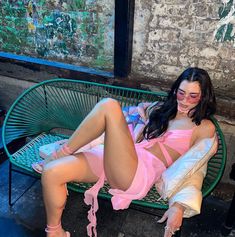 a woman laying on top of a green bench next to a brick wall and window