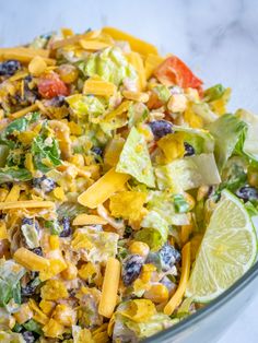 a salad with cheese, lettuce, tomatoes and black olives in a glass bowl