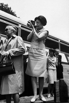 an old black and white photo of two women taking pictures in front of a bus