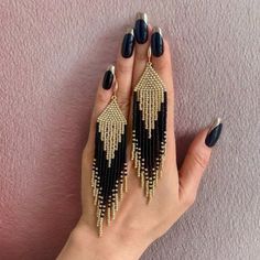 a woman's hand holding two pairs of black and gold beaded fringe earrings