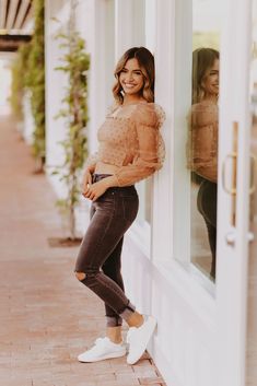 a woman leaning against the side of a building with her hands in her pockets and smiling