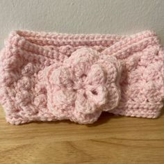 a pink crocheted headband with a flower on the side sitting on a wooden table