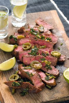 steak with olives and herbs on a cutting board next to two glasses of water