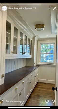 an empty kitchen with white cabinets and wood flooring in front of a large window