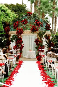 an outdoor wedding ceremony with red flowers and white linens on the aisle, surrounded by palm trees