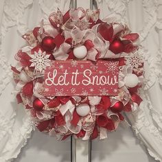 a red and white christmas wreath with let it snow written on the front, surrounded by ornaments