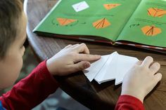 a young boy sitting at a table with an open book and paper origami