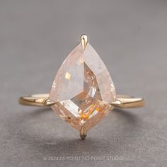 a yellow gold ring with a pear shaped peach colored diamond on the front and side