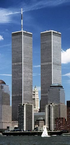 two tall buildings in the middle of a body of water with a sailboat on it