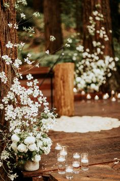 a table with candles and flowers on it in the middle of a forest filled with trees