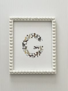 a white frame with some animals on it and a letter g in the middle that is made out of beads