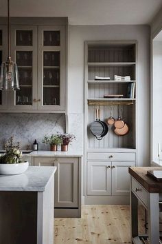 a kitchen with gray cabinets and white marble counter tops, wooden flooring and hanging pots and pans