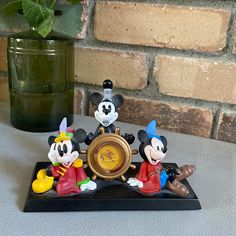 three mickey mouse figurines sitting on top of a table next to a clock