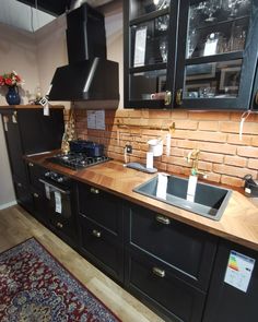 a kitchen with black cabinets and wooden counter tops, an area rug on the floor