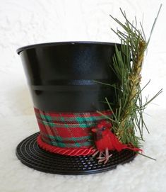 a small red bird sitting on top of a black pot with pine needles in it