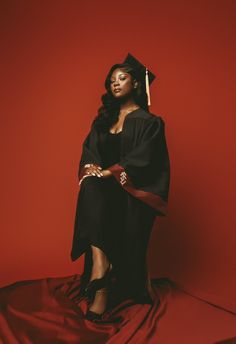 a woman in a graduation gown and cap posing for a photo on a red background