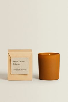 an orange candle sitting next to a box on a white surface with a label that reads mystic saffron