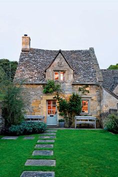 an old stone house with green grass and stepping stones leading to the front door area