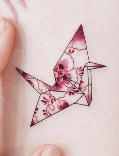 a woman's hand holding up a pink origami bird tattoo