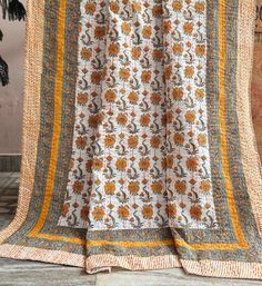 an orange and white flowered blanket hanging on a wooden wall next to a potted plant