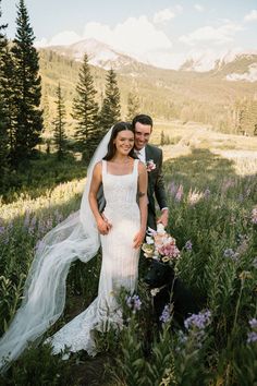 a bride and groom pose for a photo in front of mountains with wildflowers