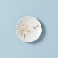 a small white plate with yellow flowers and dragonflys on the rim against a blue background