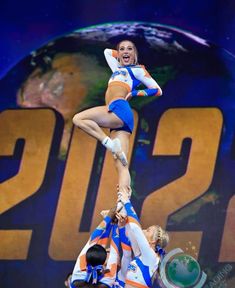 two cheerleaders performing on top of each other in front of a large screen