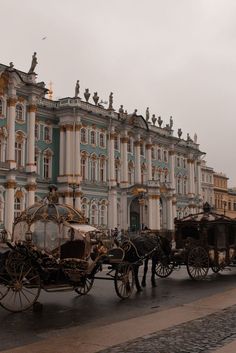 a horse drawn carriage is parked in front of a large blue and white building on a rainy day