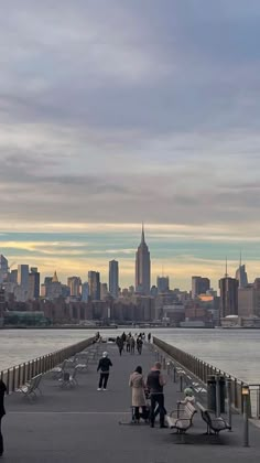 people are walking on the pier near the water and buildings in the city behind them