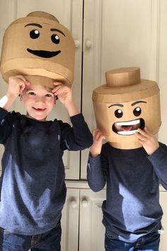 two young boys wearing paper bags with faces on them, one is covering the other's eyes