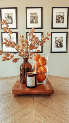 a vase filled with oranges sitting on top of a wooden table next to framed pictures