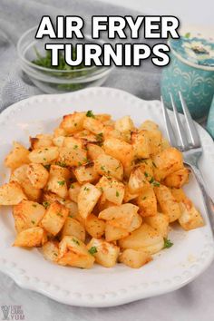 a white plate topped with potatoes and parsley next to a bowl of green vegetables