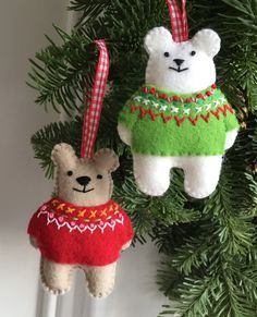 two teddy bears are hanging from a christmas ornament on a tree with red and green sweaters