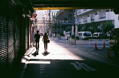 two people are walking down the street under an overpass