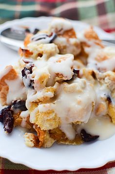 a white plate topped with dessert covered in icing and raisins next to a spoon