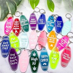 a bunch of key chains that have different colored tags on them with the words dog mom, cat mom, and happy camper written on them