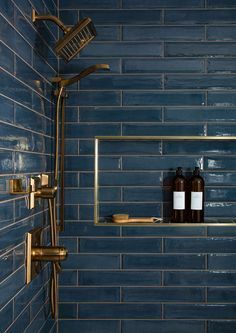 a blue tiled bathroom with gold fixtures and shower faucet, soap bottles on the shelf